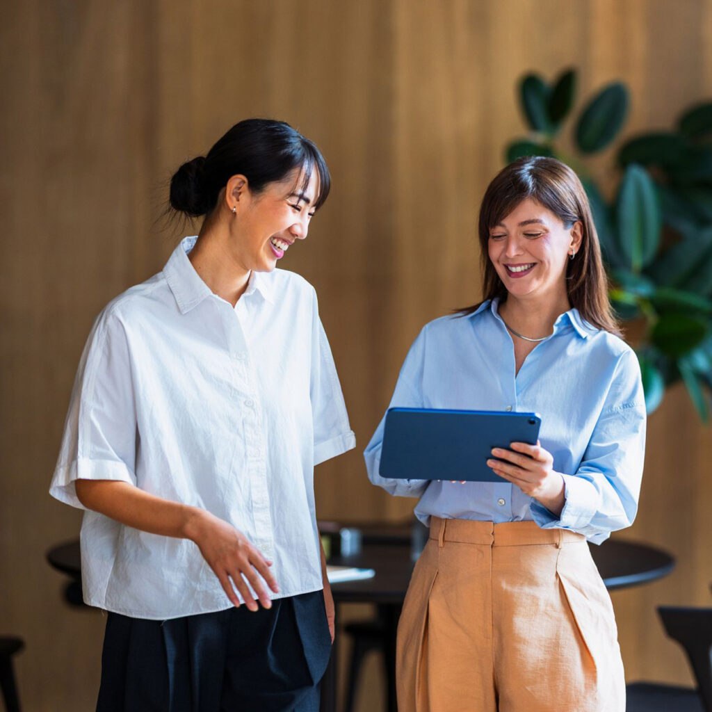 Two women sharing a moment over a tablet in a warm interior, Solance client and account director